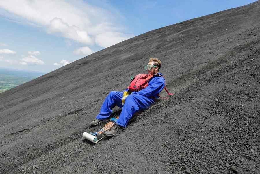 Un homme en combinaison bleue et lunettes de protection dévale une pente volcanique abrupte sur une planche.