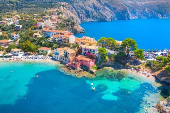 Una vista aérea de un colorido pueblo costero anidado en un acantilado, con playas y agua turquesa cristalina debajo.