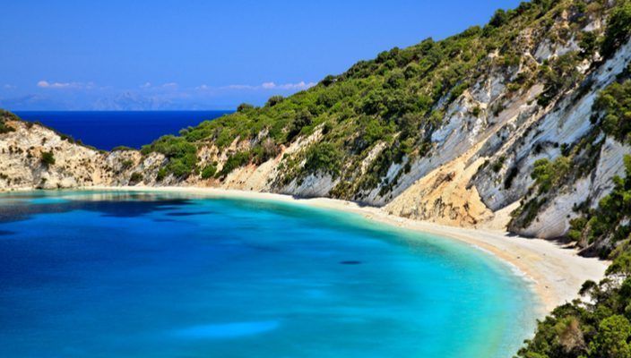 Una cala apartada con agua turquesa, una playa de arena blanca y acantilados blancos escarpados cubiertos de vegetación verde.