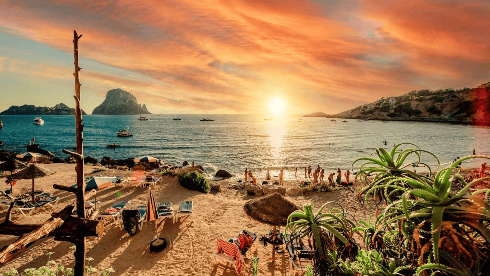 Un vivido tramonto arancione si estende su una baia serena, con persone sulla spiaggia sabbiosa, barche sull'acqua e isole rocciose all'orizzonte.