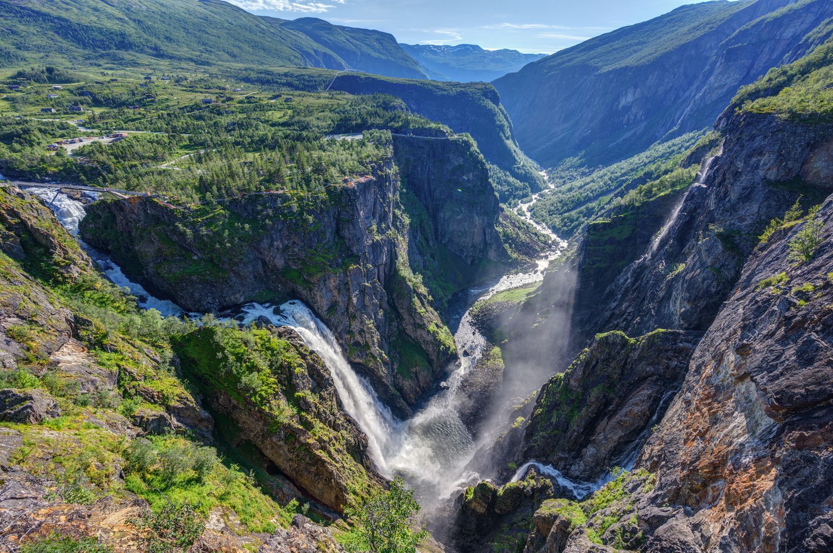 Una grande cascata si getta in un profondo canyon, con un fiume che scorre in una lussureggiante valle di montagna.