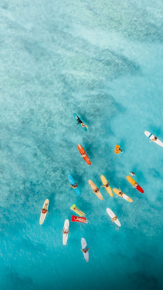 Veduta aerea di un viaggio di gruppo WeRoad su tavole da surf colorate che galleggiano in acqua limpida e turchese.