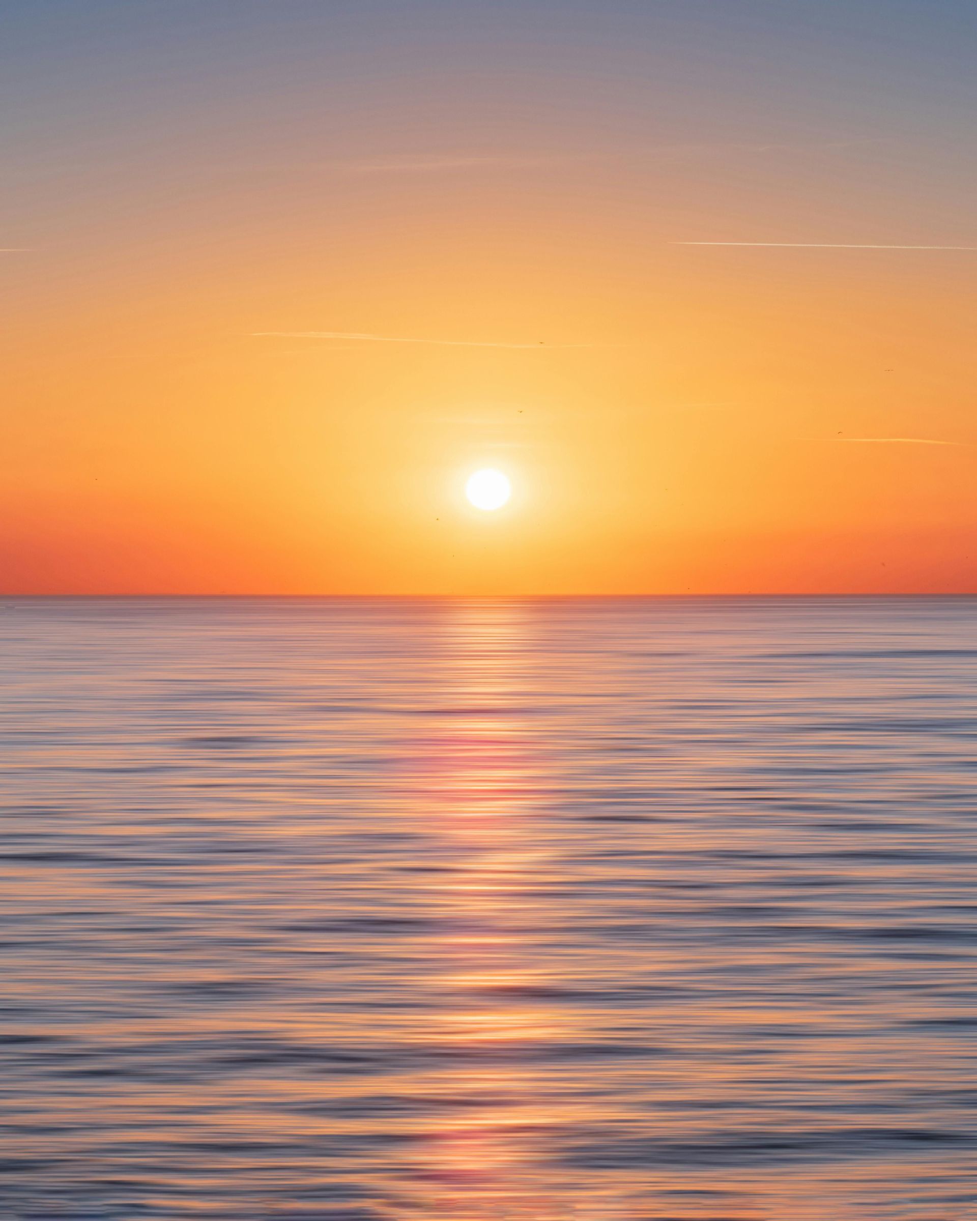 Il sole è basso all'orizzonte, diffondendo un bagliore arancione e giallo su un mare calmo con dolci increspature.