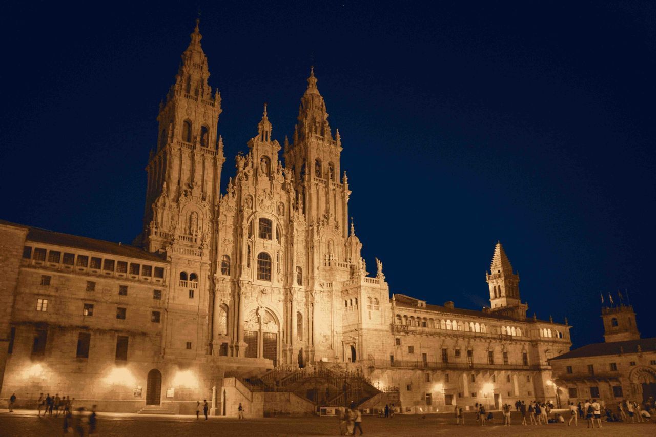 Una majestuosa y ornamentada catedral con intrincadas agujas, iluminada por luces cálidas bajo un cielo nocturno azul oscuro.