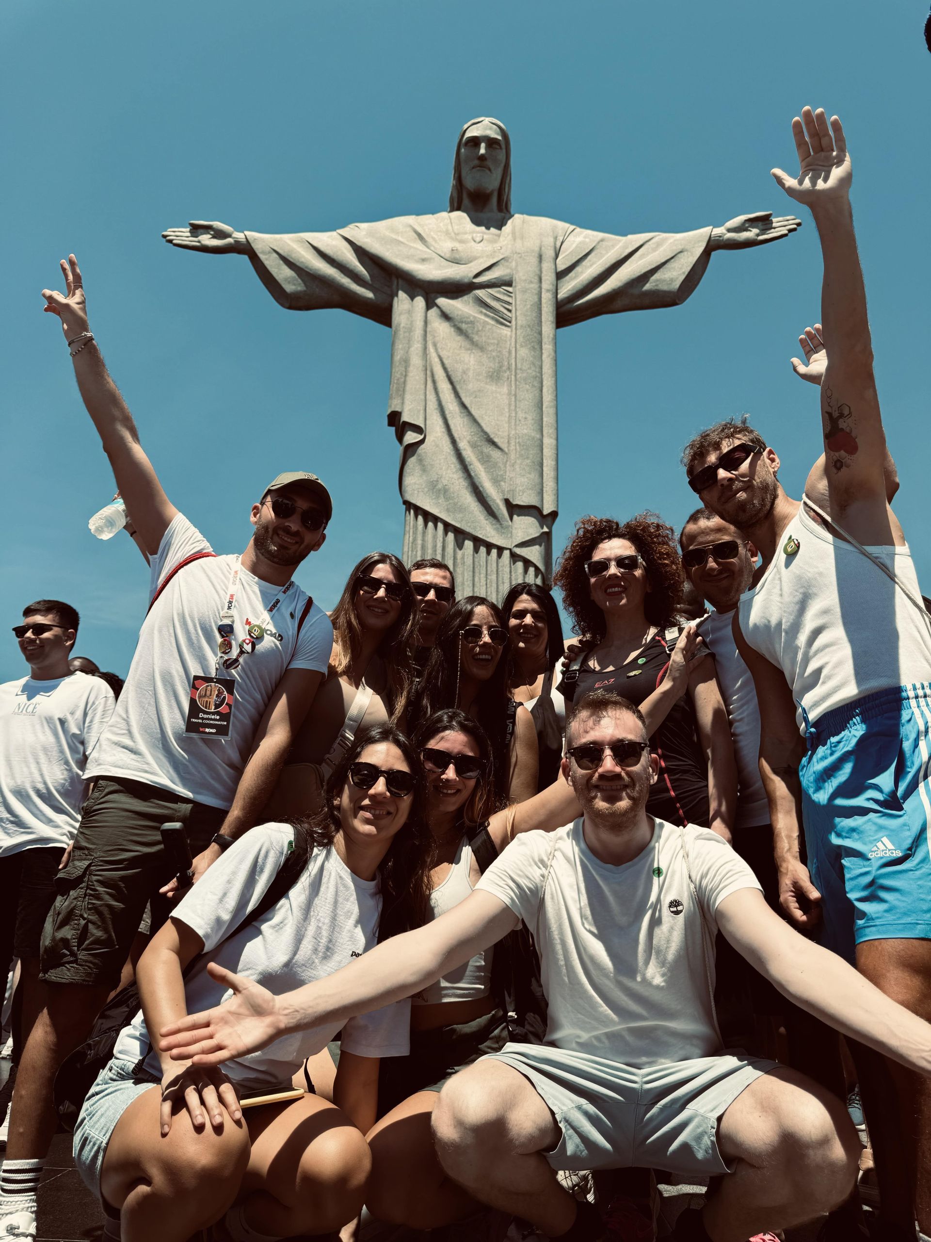 Un gruppo WeRoad sorride e posa per una foto davanti alla statua del Cristo Redentore sotto un cielo azzurro.