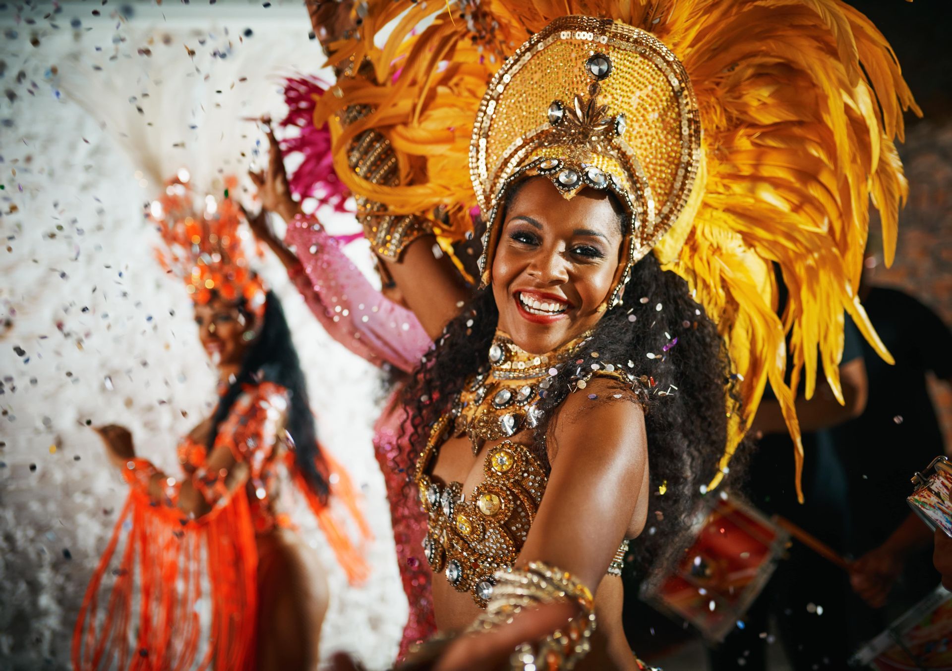 Una donna sorridente in un costume di carnevale dorato e piumato danza mentre i coriandoli le cadono intorno.