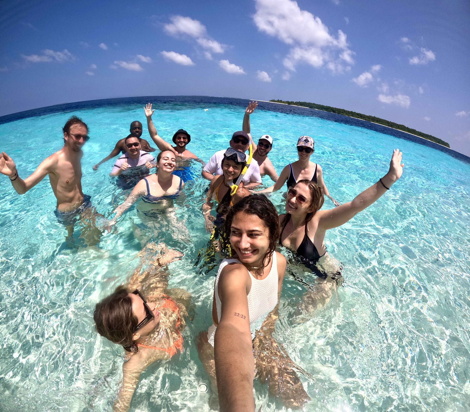 Un groupe WeRoad prend un selfie en nageant ensemble dans une eau océanique claire et turquoise sous un ciel bleu.
