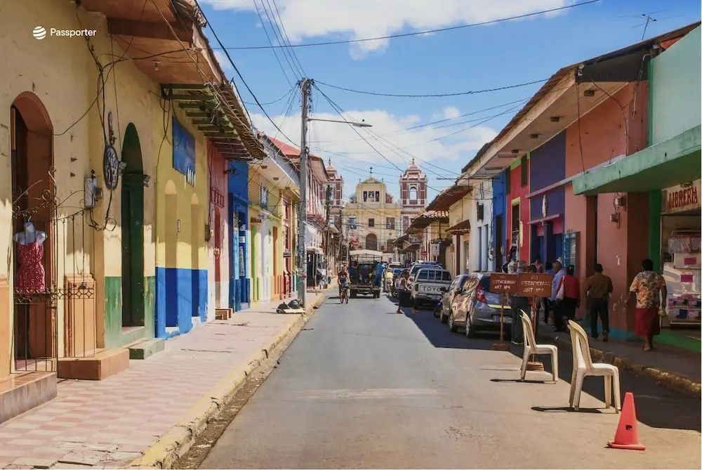Una strada fiancheggiata da colorati edifici in stile coloniale conduce verso una grande chiesa sotto un cielo azzurro.