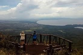 Due persone si trovano su un punto panoramico in legno che si affaccia su un vasto paesaggio con un grande lago e un cielo nuvoloso.