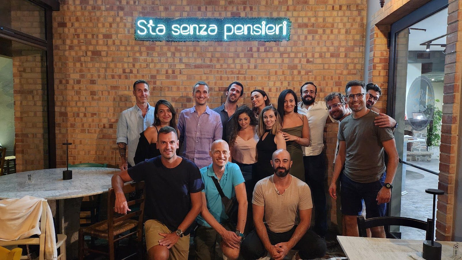 Un viaje en grupo de WeRoad posando para una foto dentro de un restaurante con una pared de ladrillo y un letrero de neón azul de fondo.