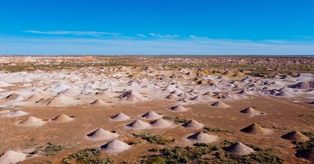 Eine weite, trockene Landschaft, übersät mit zahlreichen kleinen, kegelförmigen Erdhügeln unter einem klaren blauen Himmel.