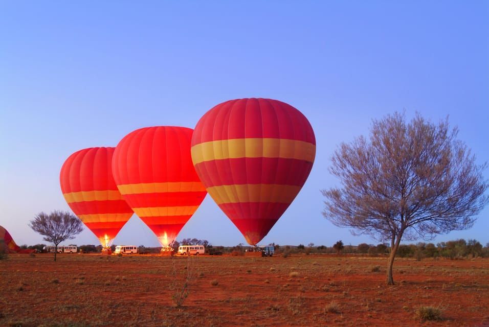 Drei rote und gelbe Heißluftballons bereiten sich bei Sonnenaufgang in einer Reihe über einer Wüstenlandschaft auf den Start vor.