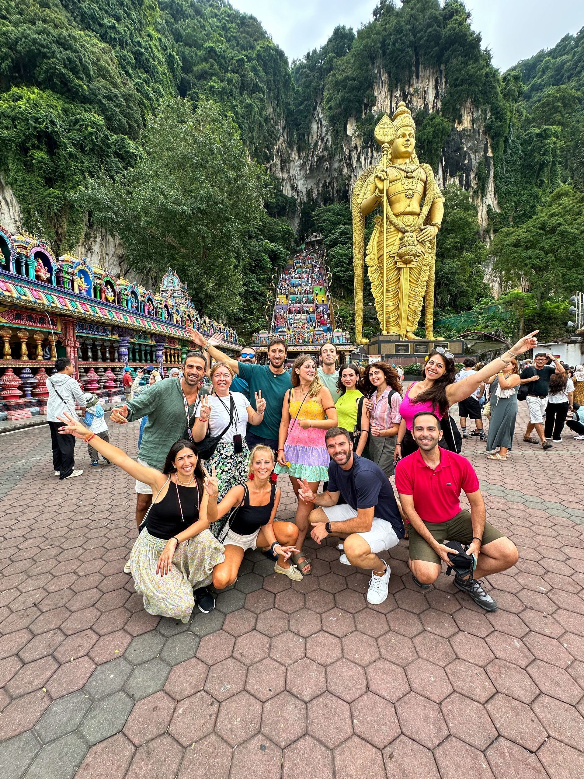 Un gruppo WeRoad posa per una foto davanti a una statua dorata gigante e un tempio colorato alla base di una scogliera boscosa.
