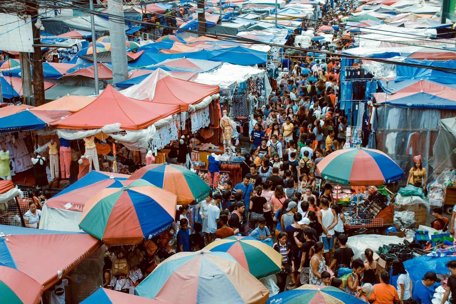 Una vista aérea de un bullicioso mercado callejero al aire libre abarrotado de gente, sombrillas coloridas y puestos de vendedores.