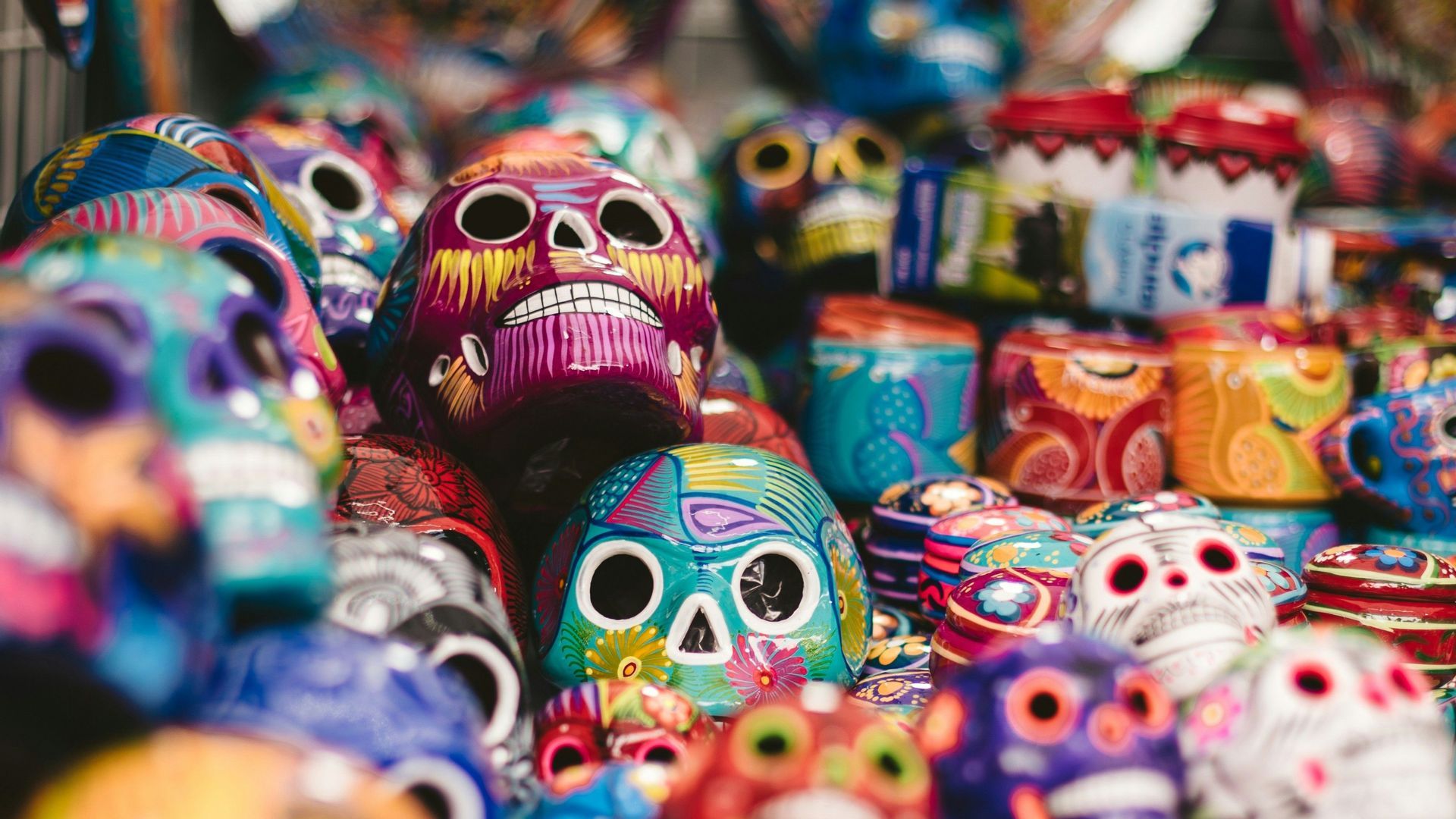 Eine Sammlung von bunten, detailreich bemalten Calavera-Schädeln, dicht aneinander ausgestellt.