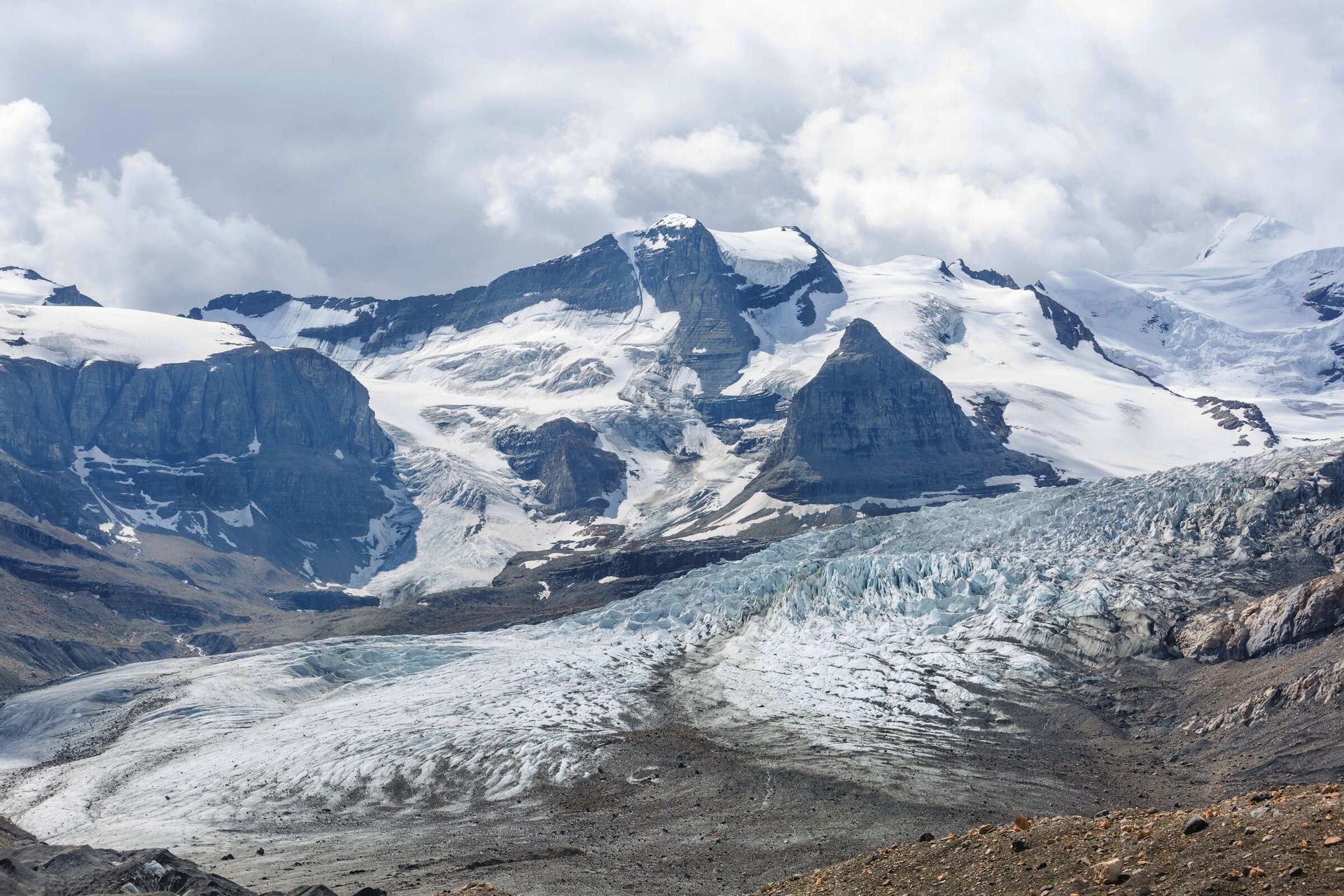 Ein großer Gletscher fließt von schneebedeckten Bergen unter bewölktem Himmel ein Tal hinab.