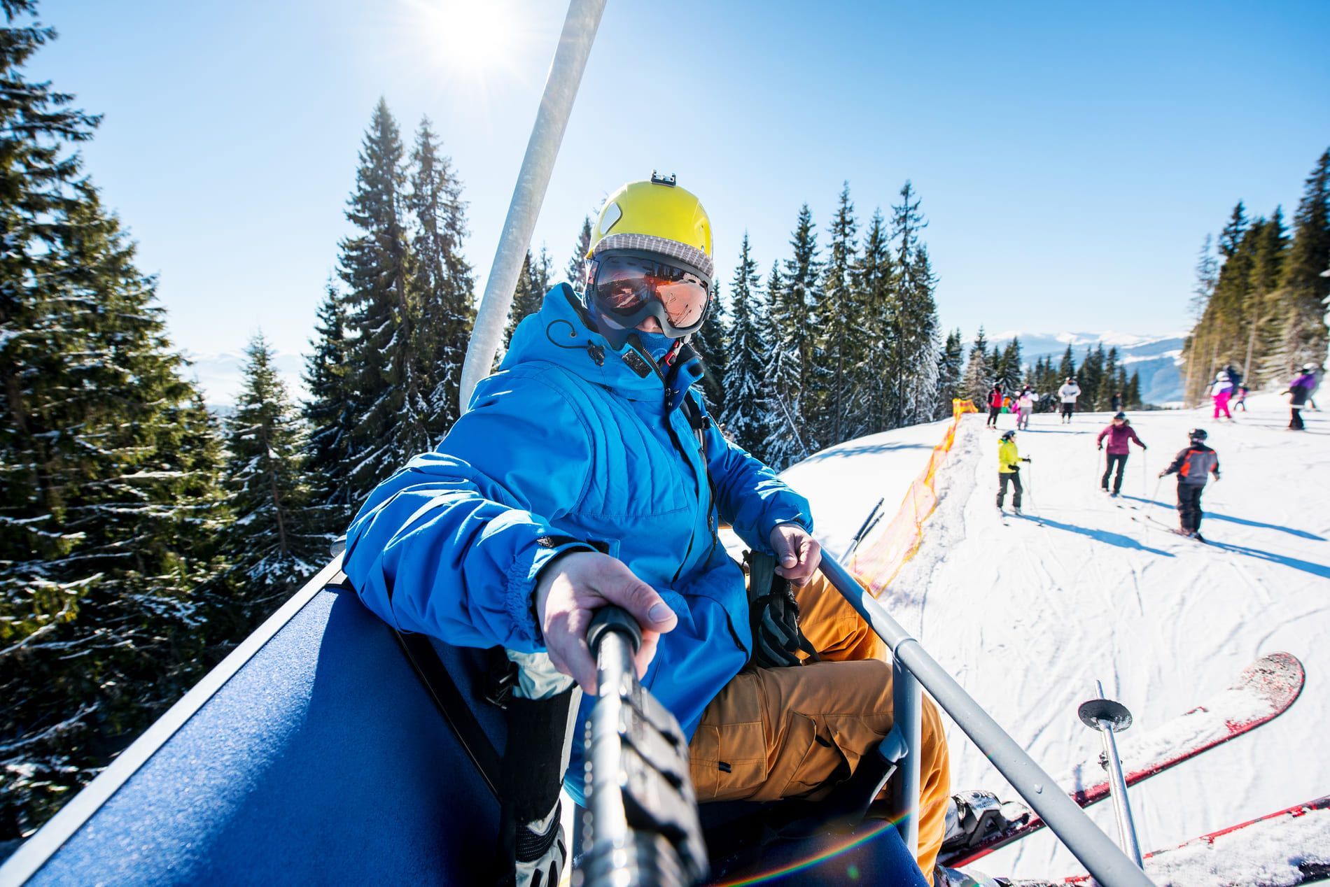 Eine Person einer WeRoad-Gruppenreise macht ein Selfie im Skilift, während sie über einen sonnigen, schneebedeckten Hang mit Kiefern fährt.