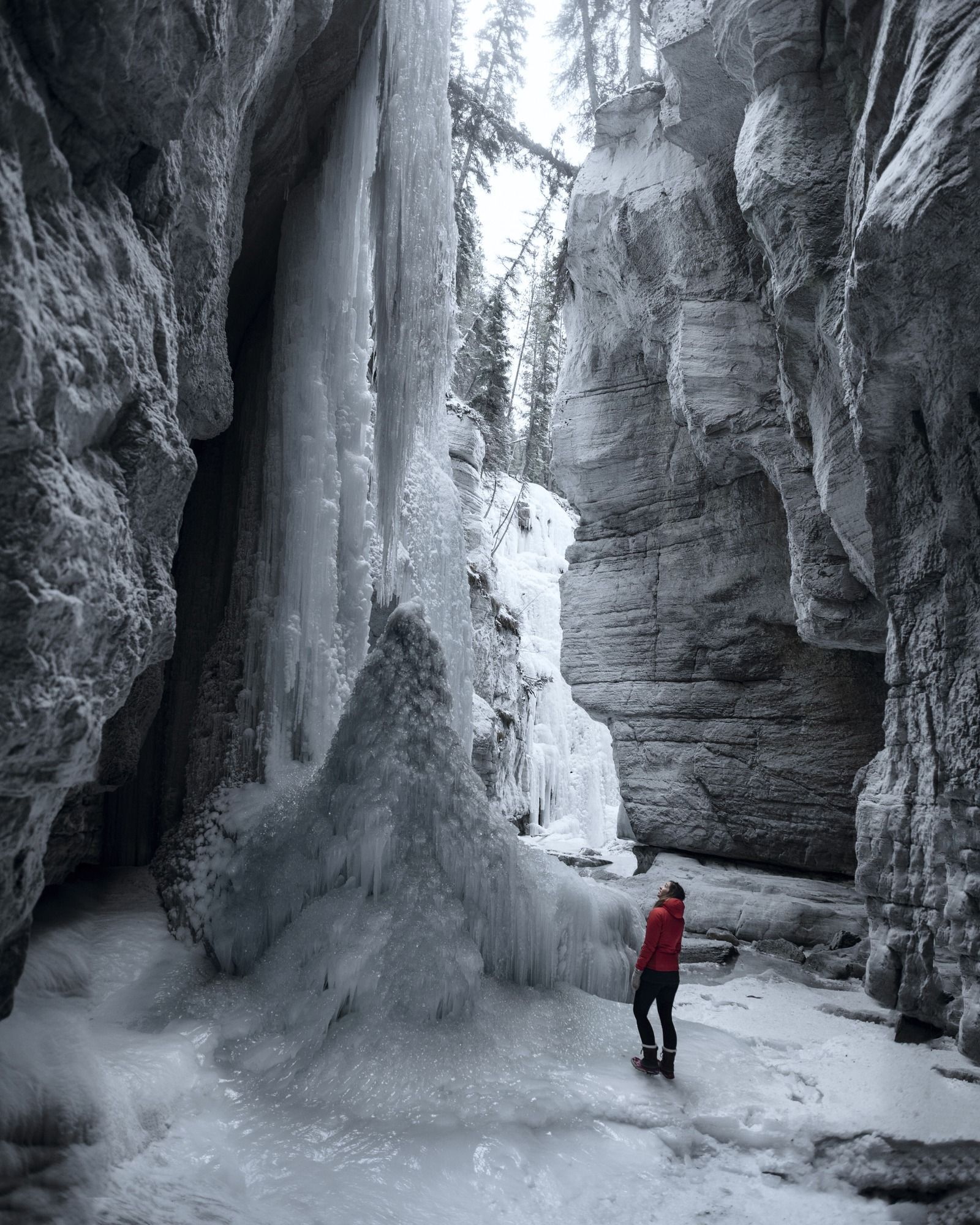Eine Person in roter Jacke steht in einer engen, eisigen Schlucht und blickt zu einem großen gefrorenen Wasserfall auf.