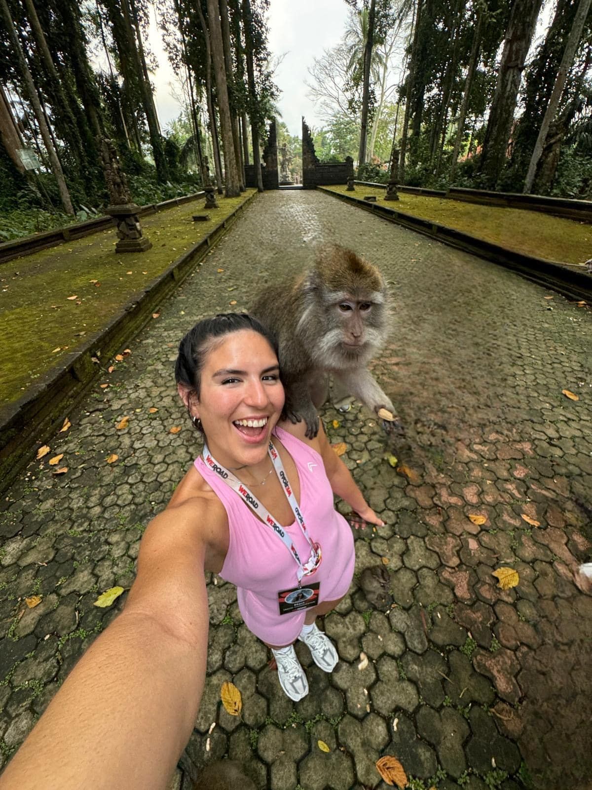 Eine Frau auf einer WeRoad-Reise lächelt, während sie auf einem gepflasterten Weg ein Selfie mit einem Affen auf ihrer Schulter macht.