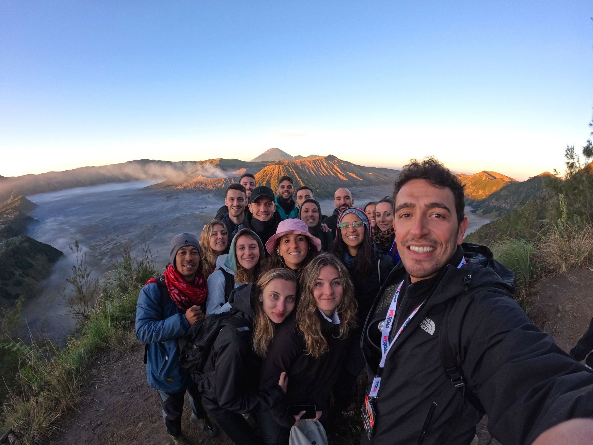 Un groupe WeRoad prend un selfie sur un point de vue, avec un paysage de caldeira volcanique en arrière-plan au lever du soleil.