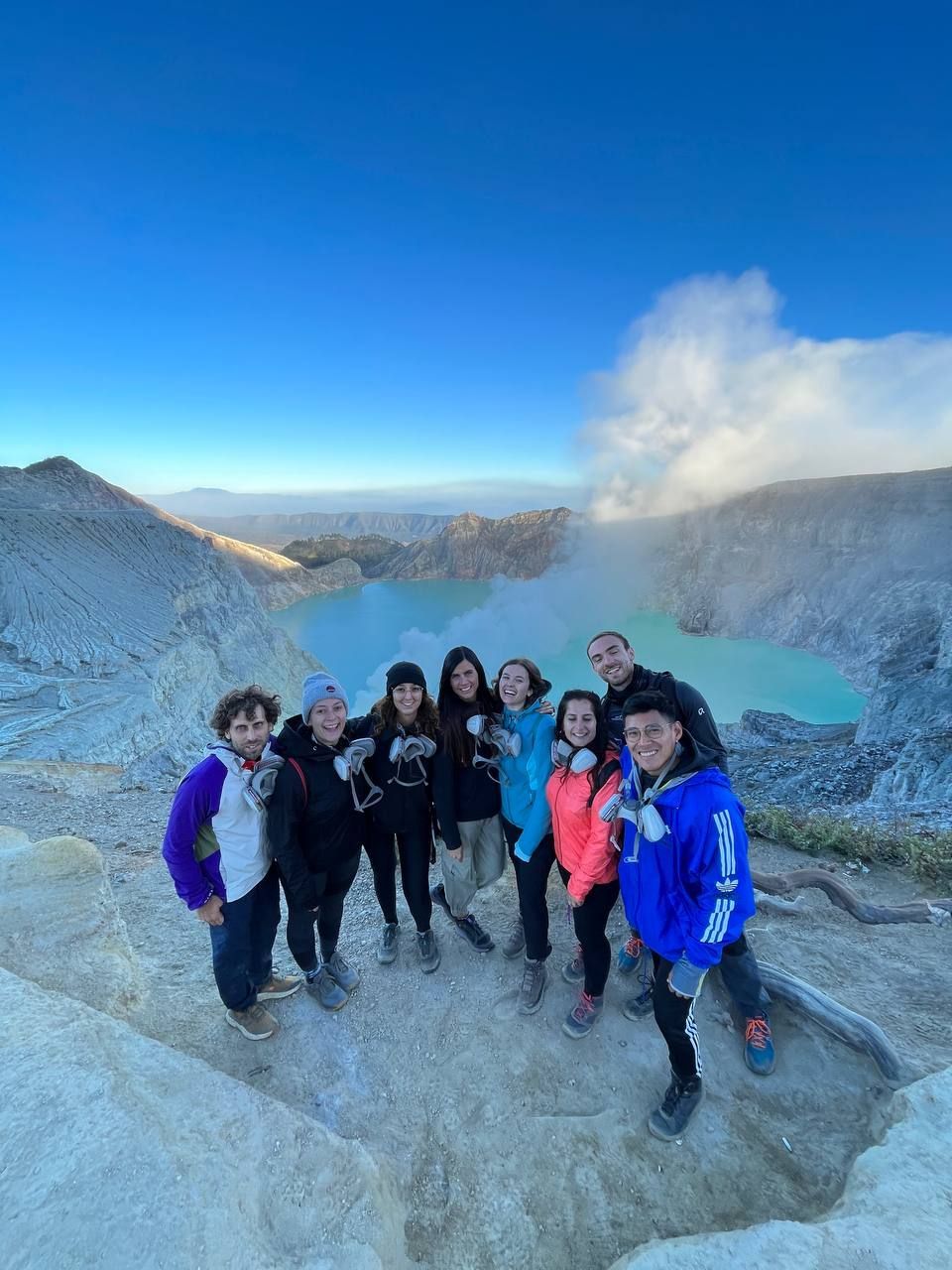 Un grupo de WeRoad posa para una foto al borde de un cráter volcánico, con un lago turquesa brillante de fondo.