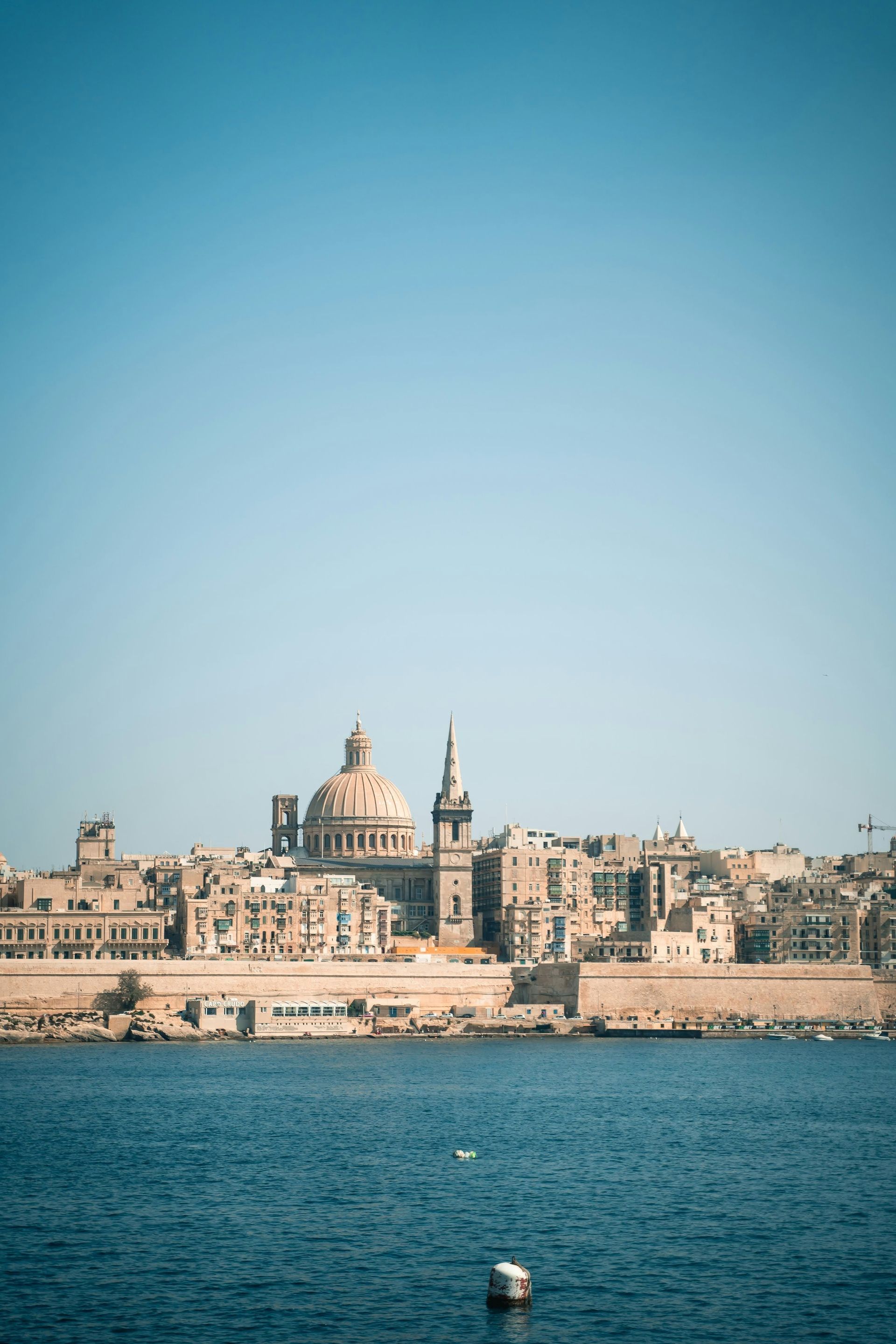 Une ville côtière avec un dôme et une flèche proéminents vus depuis l'eau bleue sous un ciel clair.