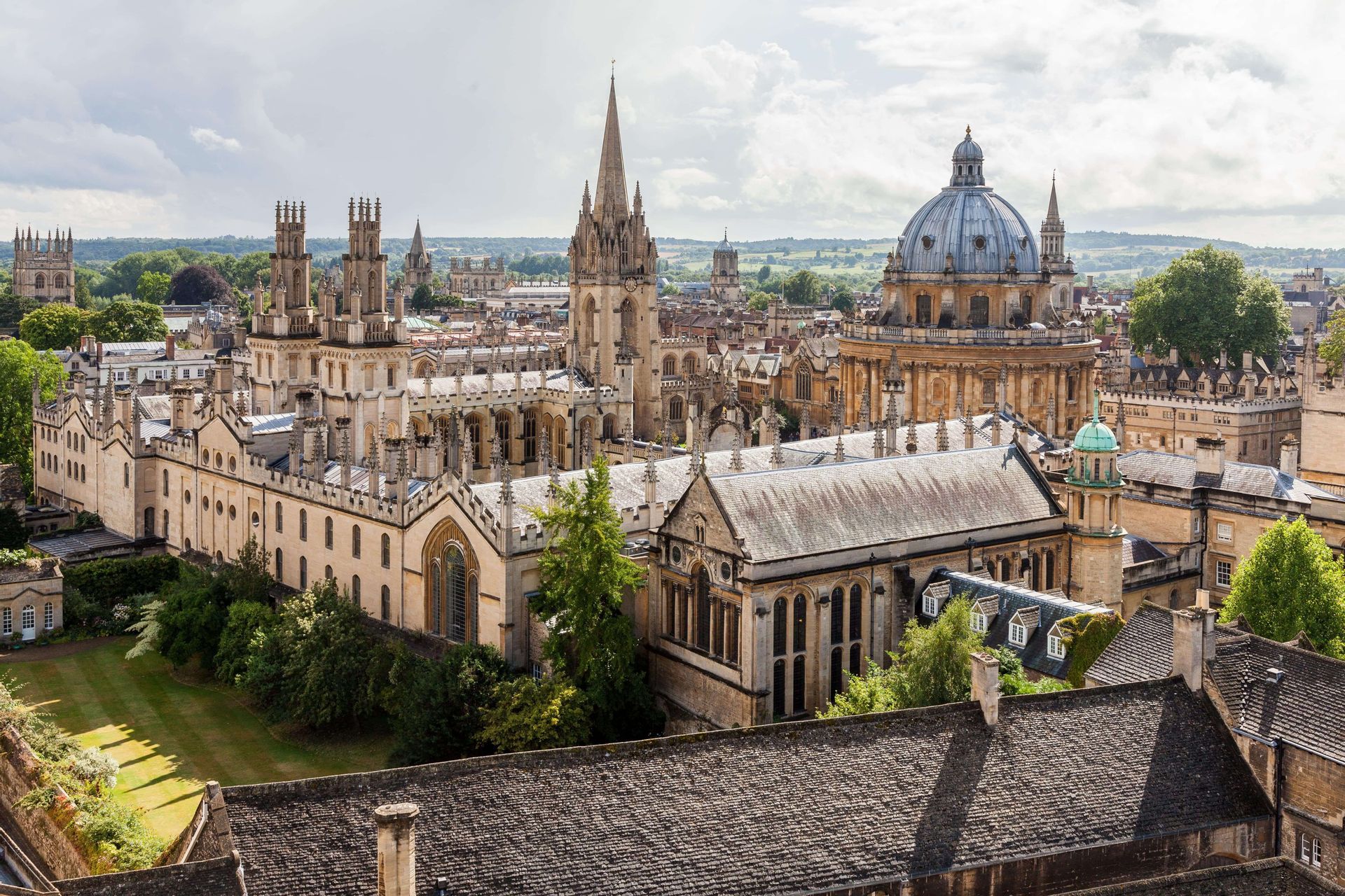 A historic city skyline with Gothic university buildings, prominent spires, and a large central dome.