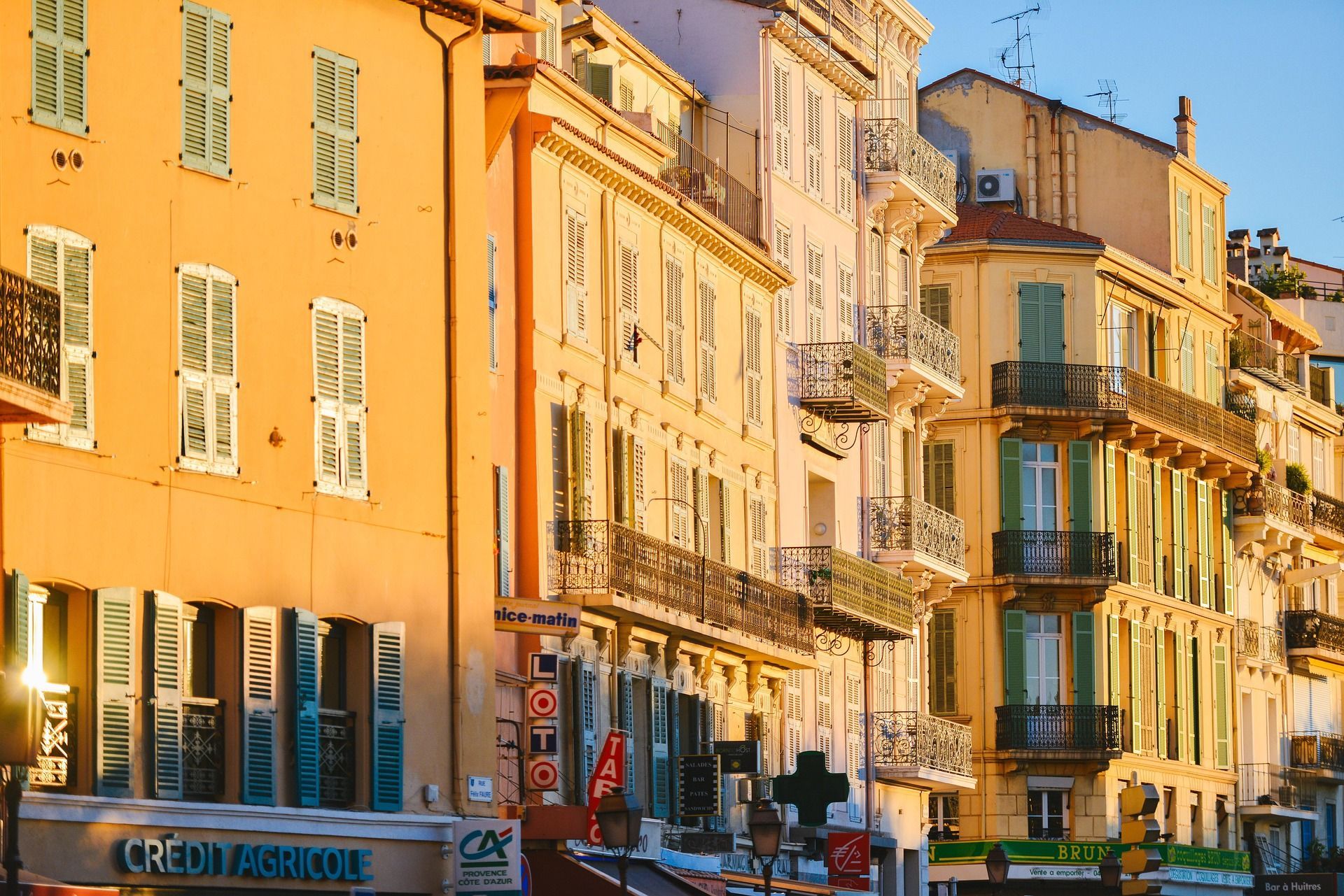Una hilera de edificios coloridos con persianas y balcones se baña en la luz dorada del atardecer en una calle de la ciudad.