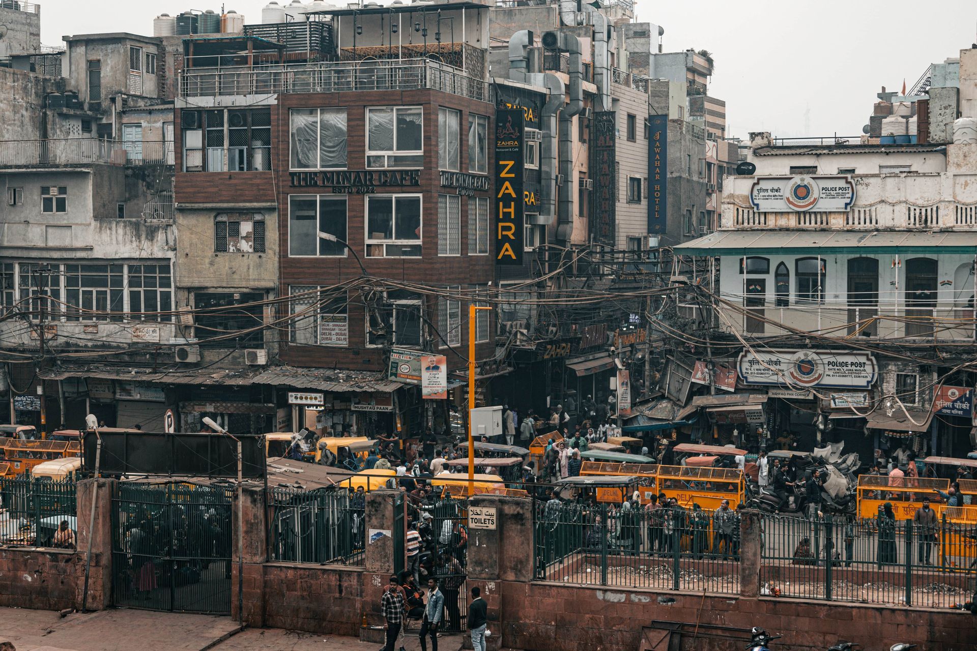 Une vue aérienne d'une rue de ville animée, bondée de piétons, de pousse-pousse jaunes et de bâtiments denses et patinés.