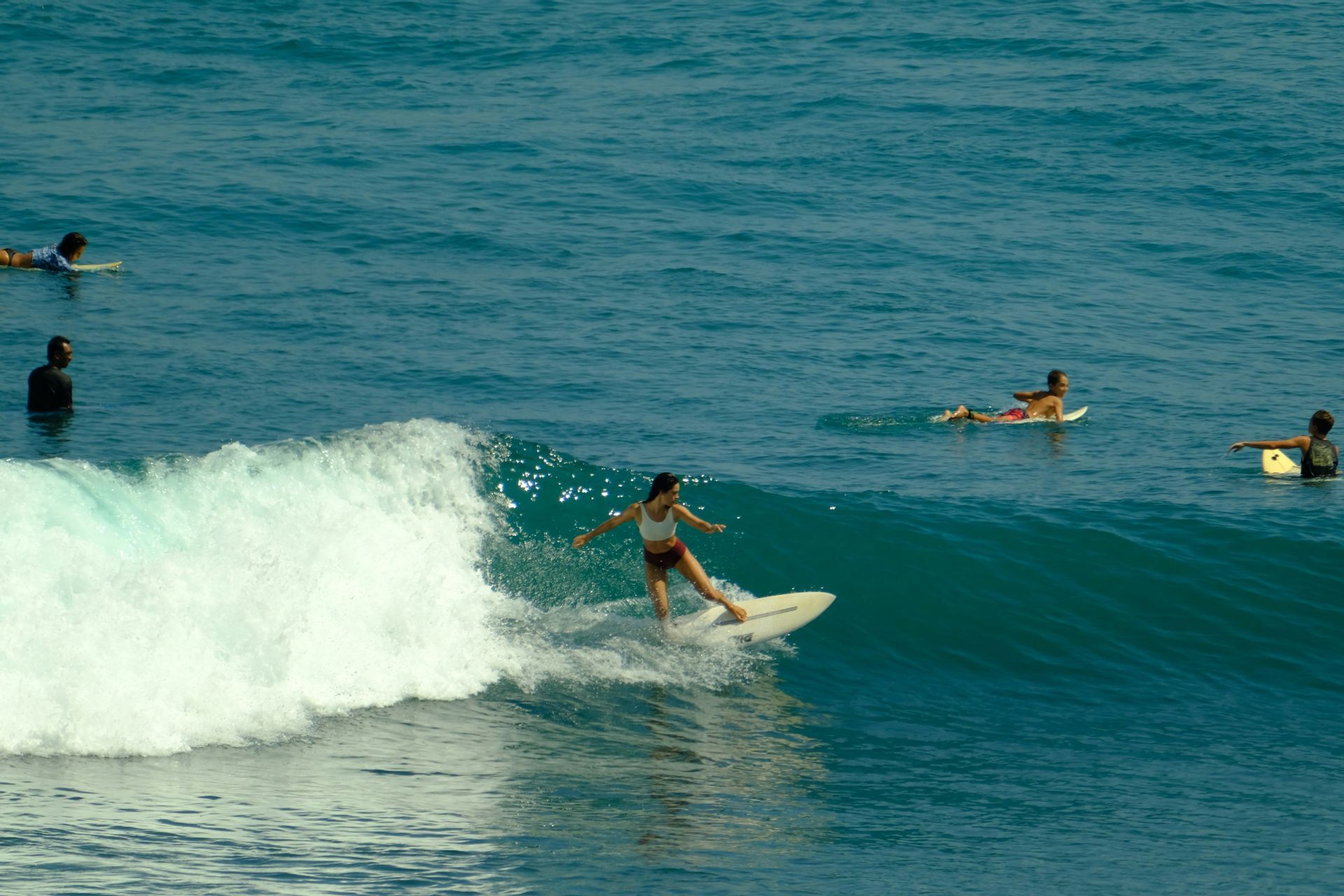 Una donna di un viaggio di gruppo WeRoad cavalca un'onda blu mentre altre persone su tavole da surf aspettano nell'oceano.