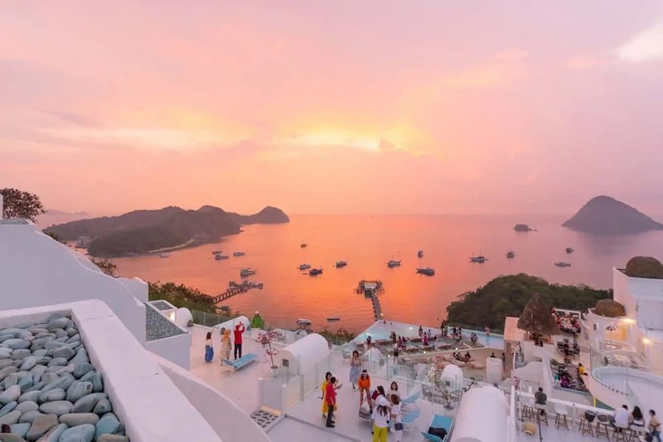 Un groupe WeRoad observe le coucher de soleil depuis une terrasse de toit blanche, surplombant une baie avec des bateaux et des îles.