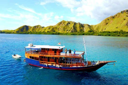 Un voyage de groupe WeRoad sur un bateau en bois à deux ponts dans des eaux calmes et turquoise, avec des îles vertes et vallonnées en arrière-plan.