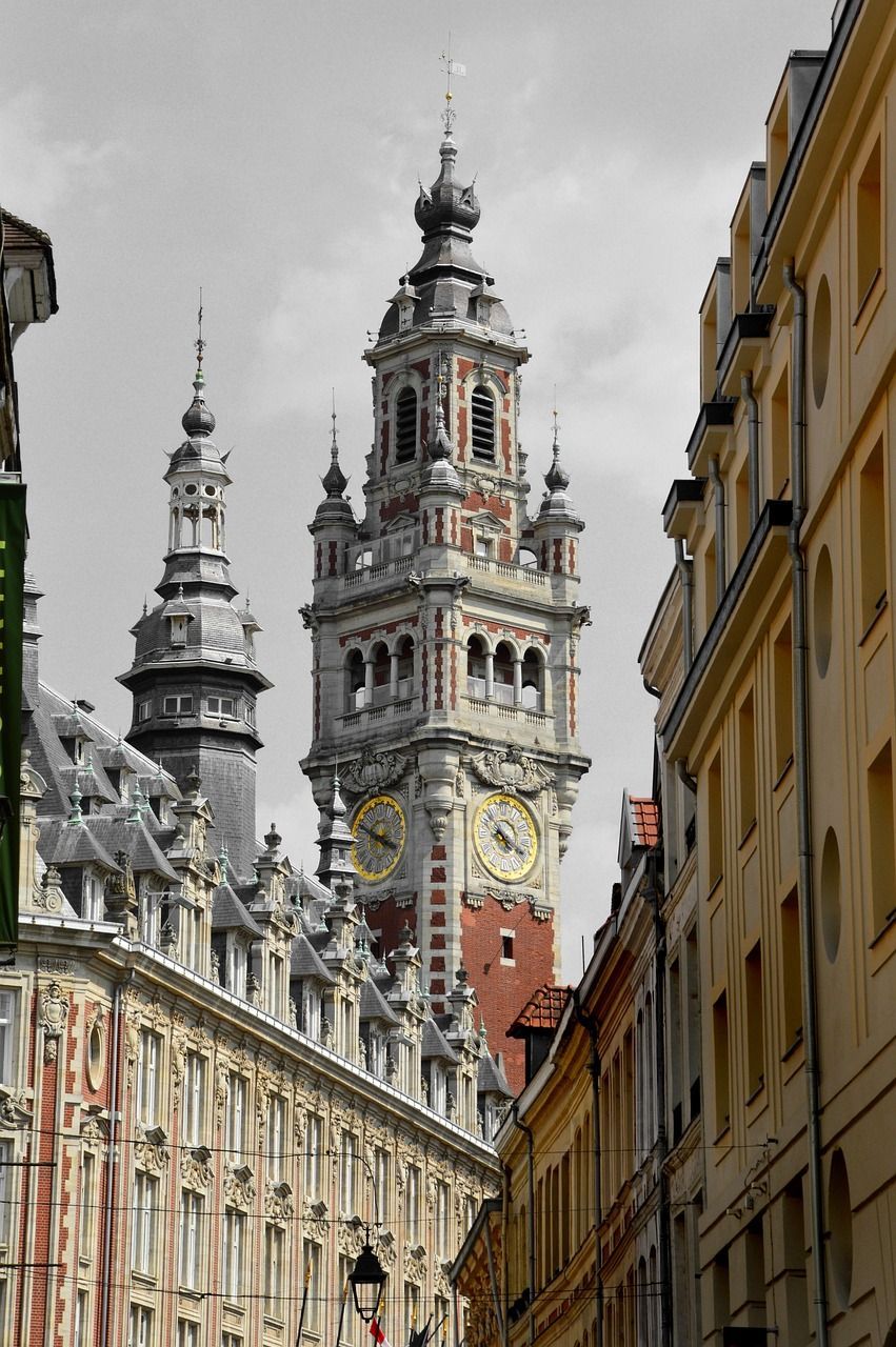 Une image aux couleurs sélectives d'une tour horloge ornée en briques rouges avec des cadrans dorés, encadrée par des bâtiments sur un ciel gris monochrome.