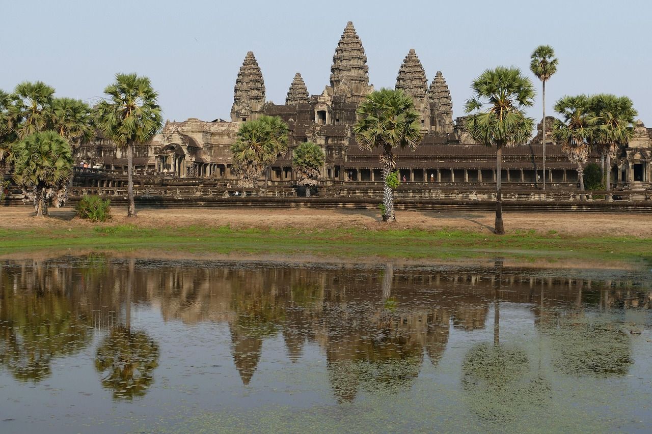 Un ancien temple de pierre avec plusieurs tours et des palmiers se reflète dans une étendue d'eau calme au premier plan.