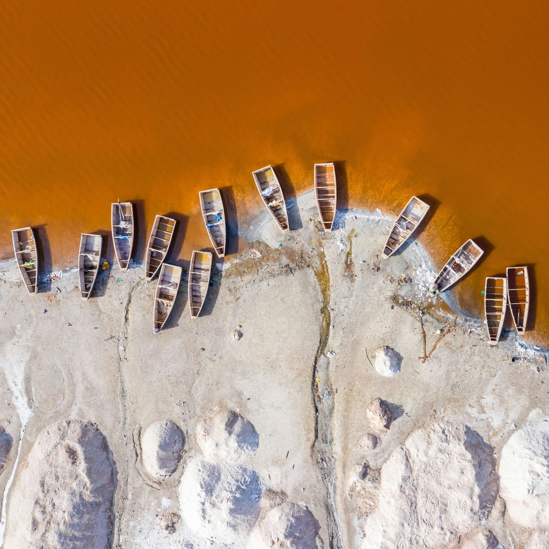 Vue aérienne de bateaux en bois sur la rive d'un lac orange près de tas de sel blanc.