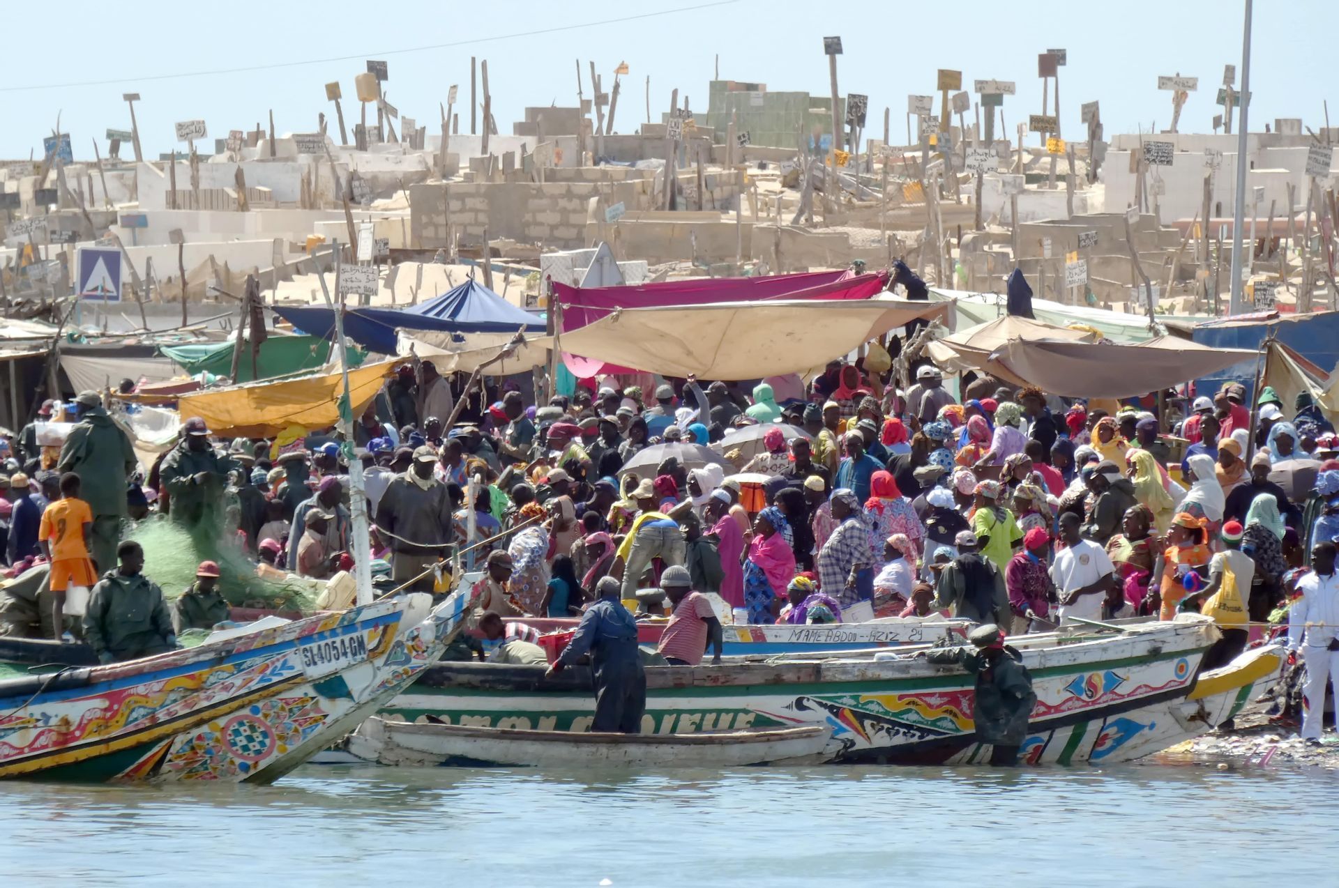 Un marché animé au bord de l'eau avec une foule nombreuse et des bateaux de pêche colorés amarrés le long du rivage.