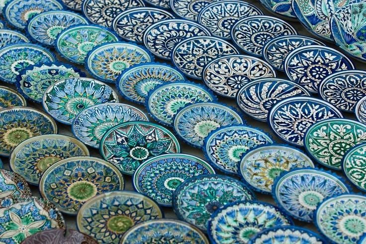 Des dizaines d'assiettes en céramique peintes à la main avec des motifs géométriques complexes bleus et verts sont exposées en rangées superposées.