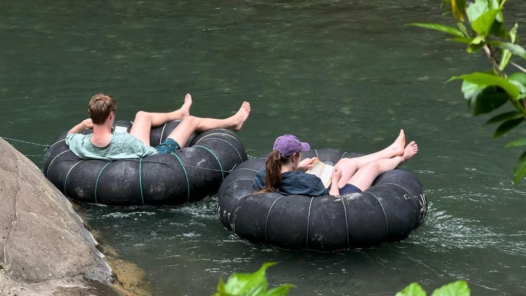 Due persone di un viaggio di gruppo WeRoad leggono libri mentre si rilassano su ciambelle in un fiume.