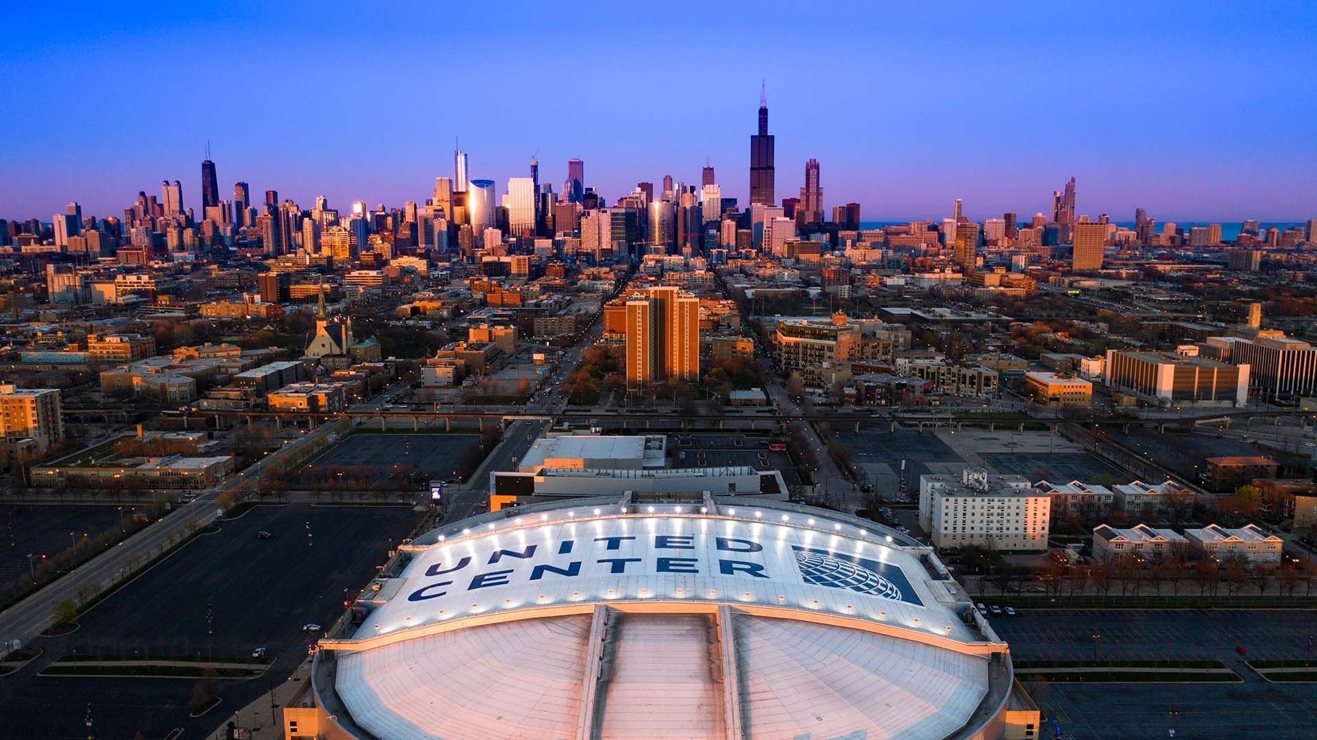 Una vista aerea del tetto a cupola dello United Center con lo skyline di Chicago visibile sullo sfondo contro un cielo crepuscolare.