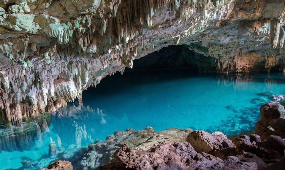 Une grande caverne souterraine abritant un bassin d'eau turquoise limpide, avec de nombreuses stalactites pendant du plafond.