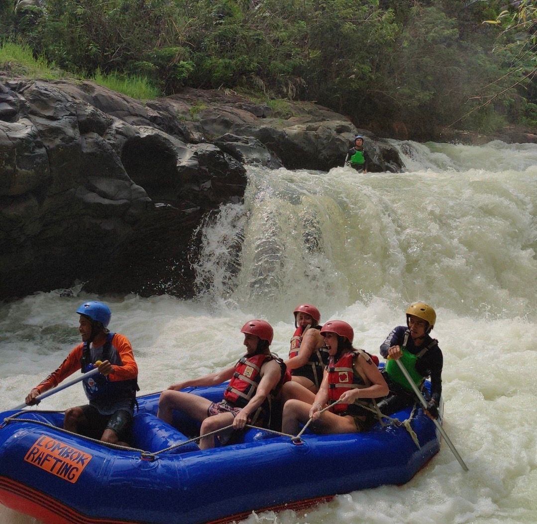 Eine WeRoad Gruppenreise Wildwasser-Rafting in einem blauen Schlauchboot auf einem Fluss mit Stromschnellen und einem Wasserfall.