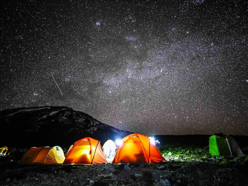 Illuminated tents at a campsite on rocky ground under a night sky full of stars and the Milky Way.