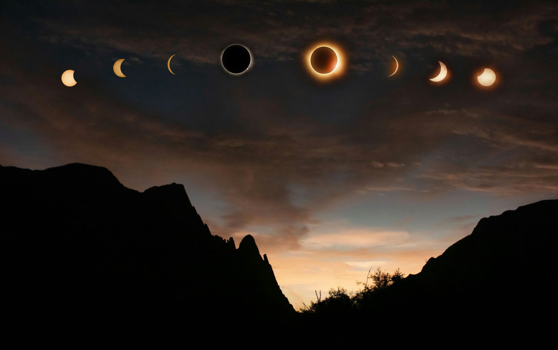 Die Phasen einer Sonnenfinsternis bilden einen Bogen am bewölkten Himmel über einer silhouettierten Bergkette in der Dämmerung.