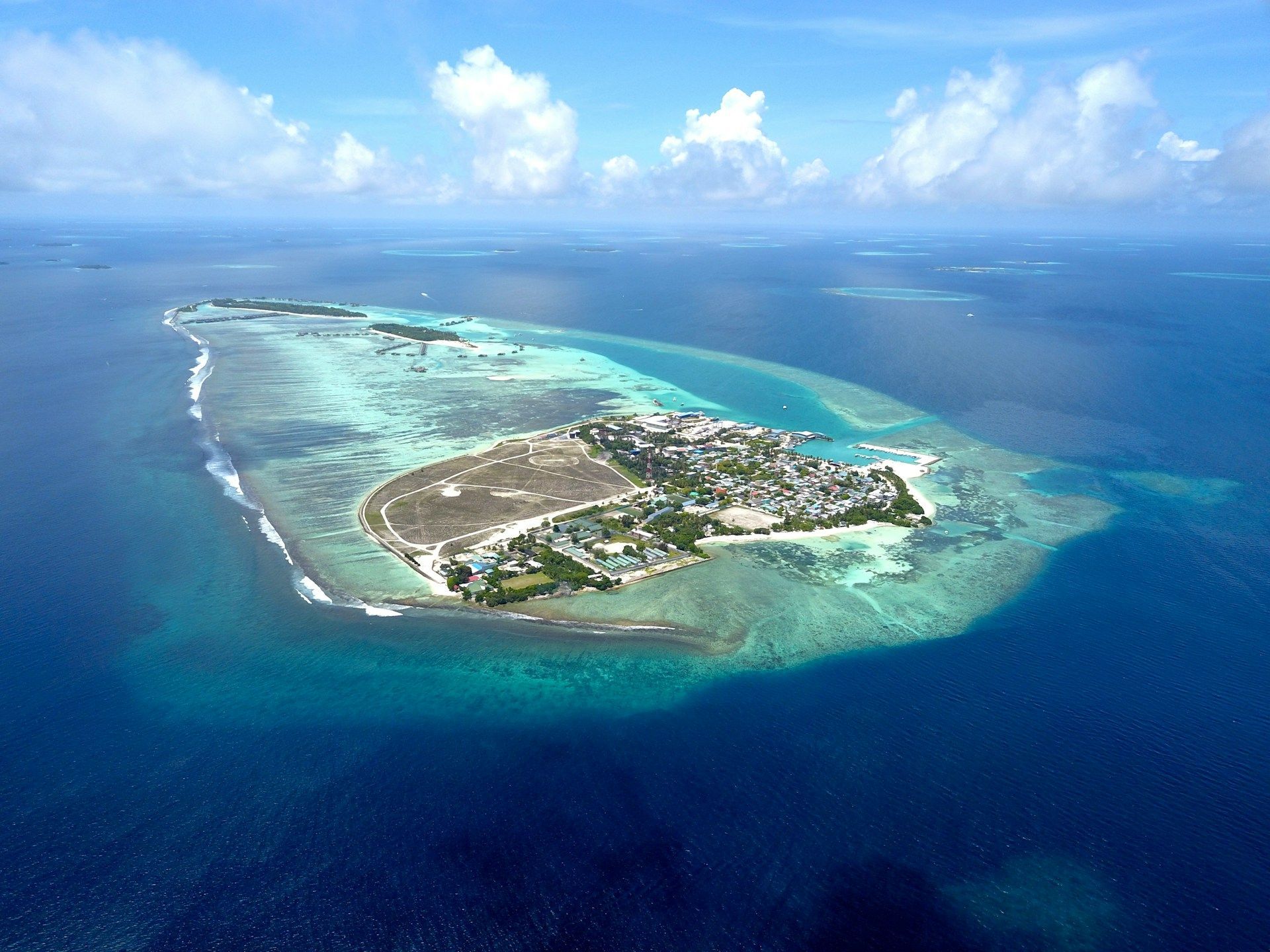 Vista aérea de un atolón isleño poblado con un arrecife de coral circundante, ubicado en aguas oceánicas turquesas y azul profundo.