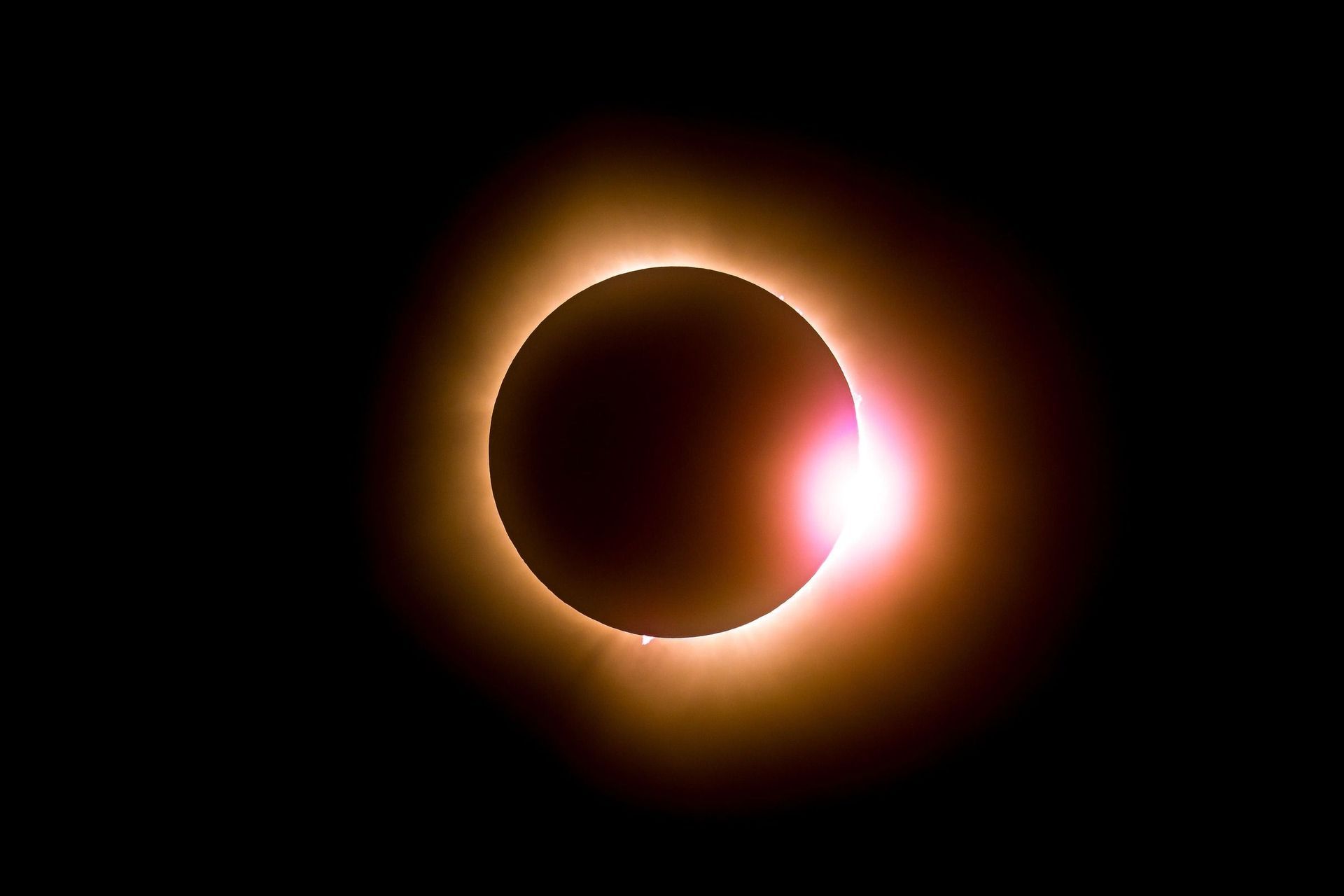 Der Mond erzeugt eine totale Sonnenfinsternis, wobei die Korona der Sonne und der Diamantring-Effekt vor einem schwarzen Himmel sichtbar sind.