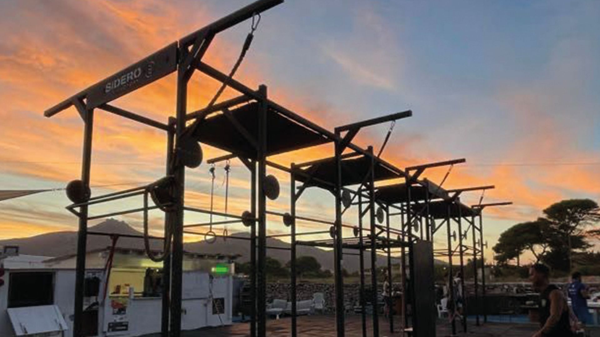 Una palestra all'aperto con stazioni di allenamento multiple, stagliata contro un vibrante cielo al tramonto con nuvole rosa e arancioni.
