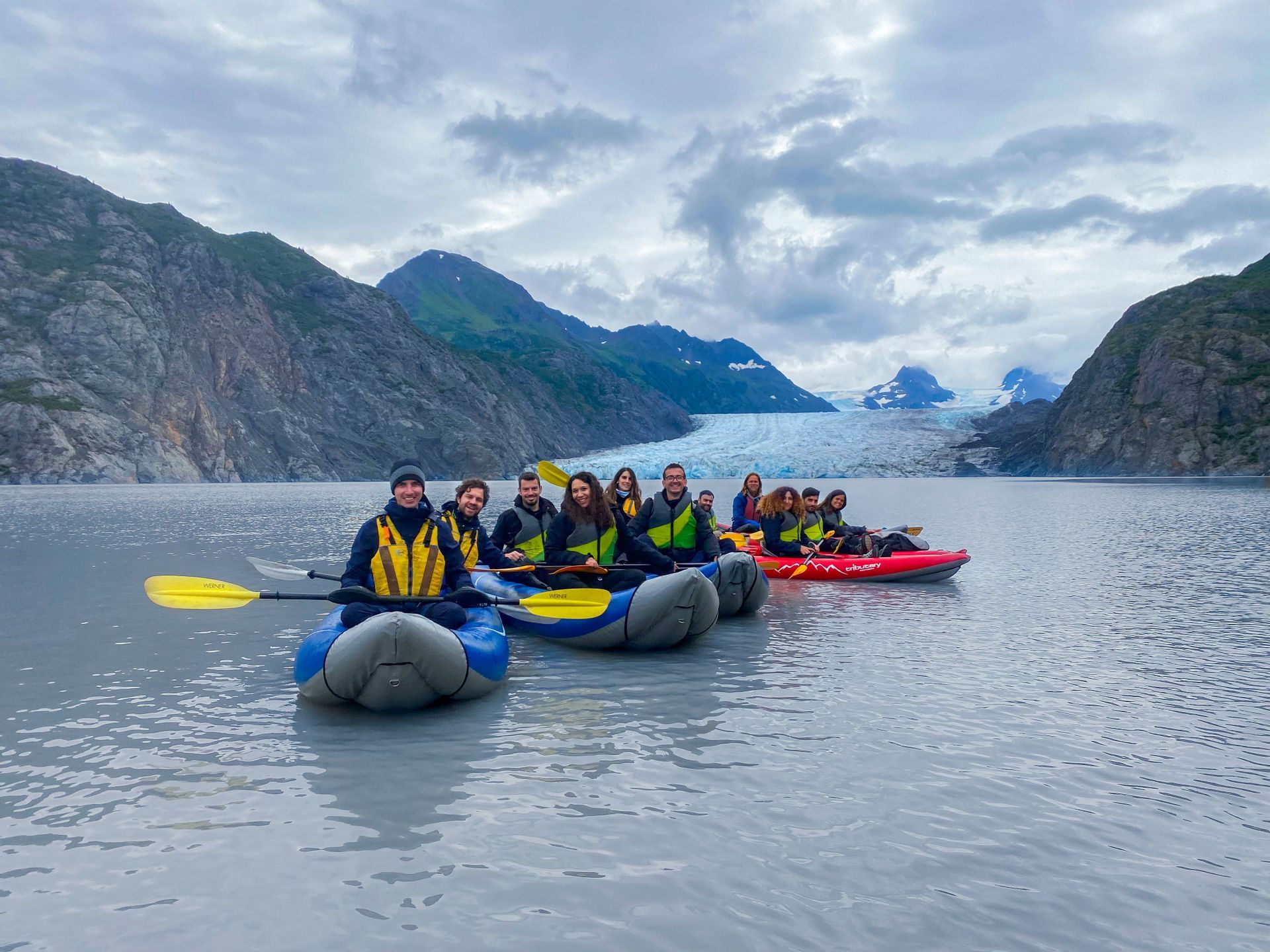 Eine WeRoad Gruppenreise beim Kajakfahren auf einem ruhigen See, mit einem großen Gletscher und Bergen in der Ferne.