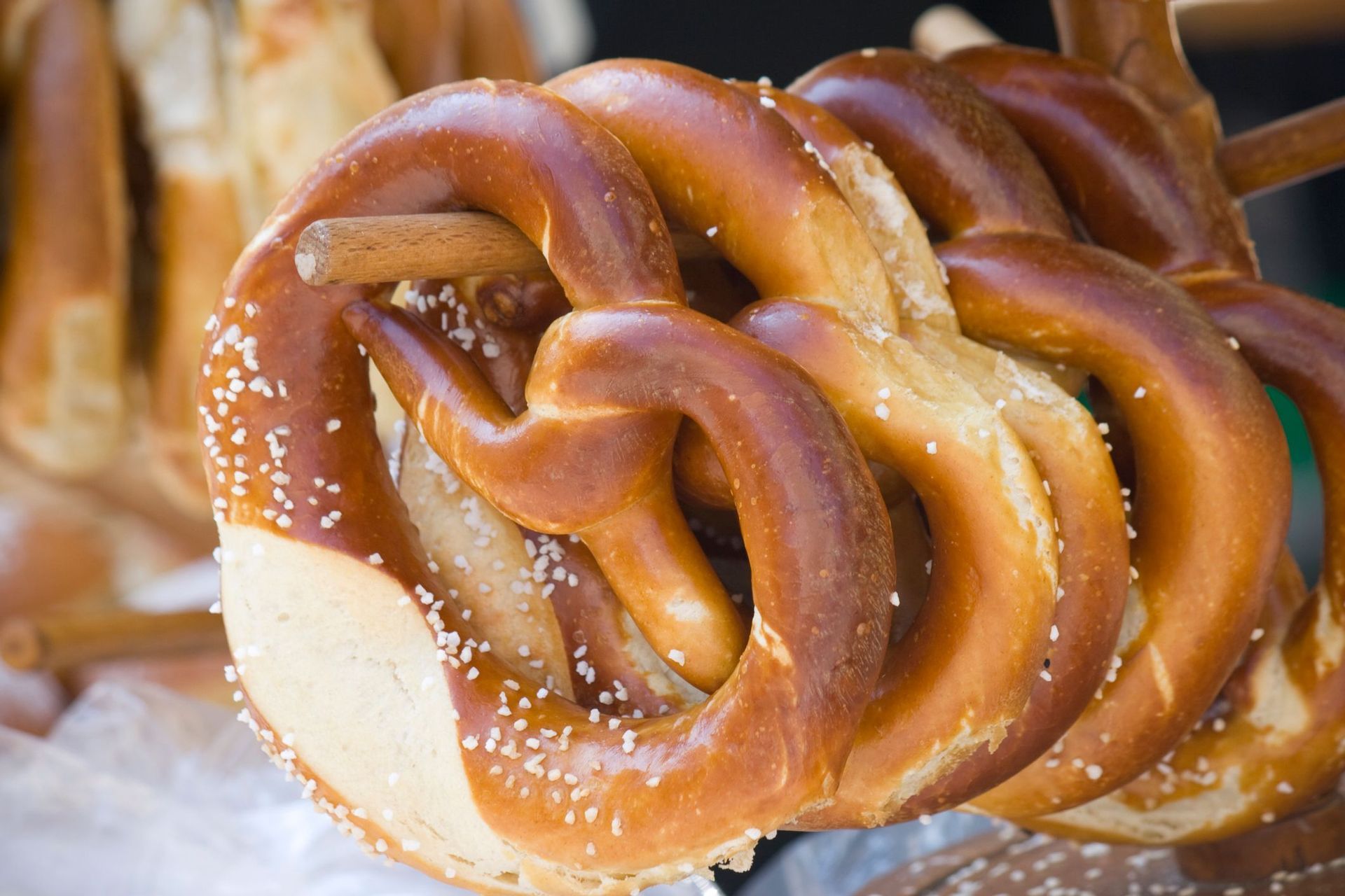 A close-up of several soft pretzels sprinkled with coarse salt hanging on a wooden display stand at a market.