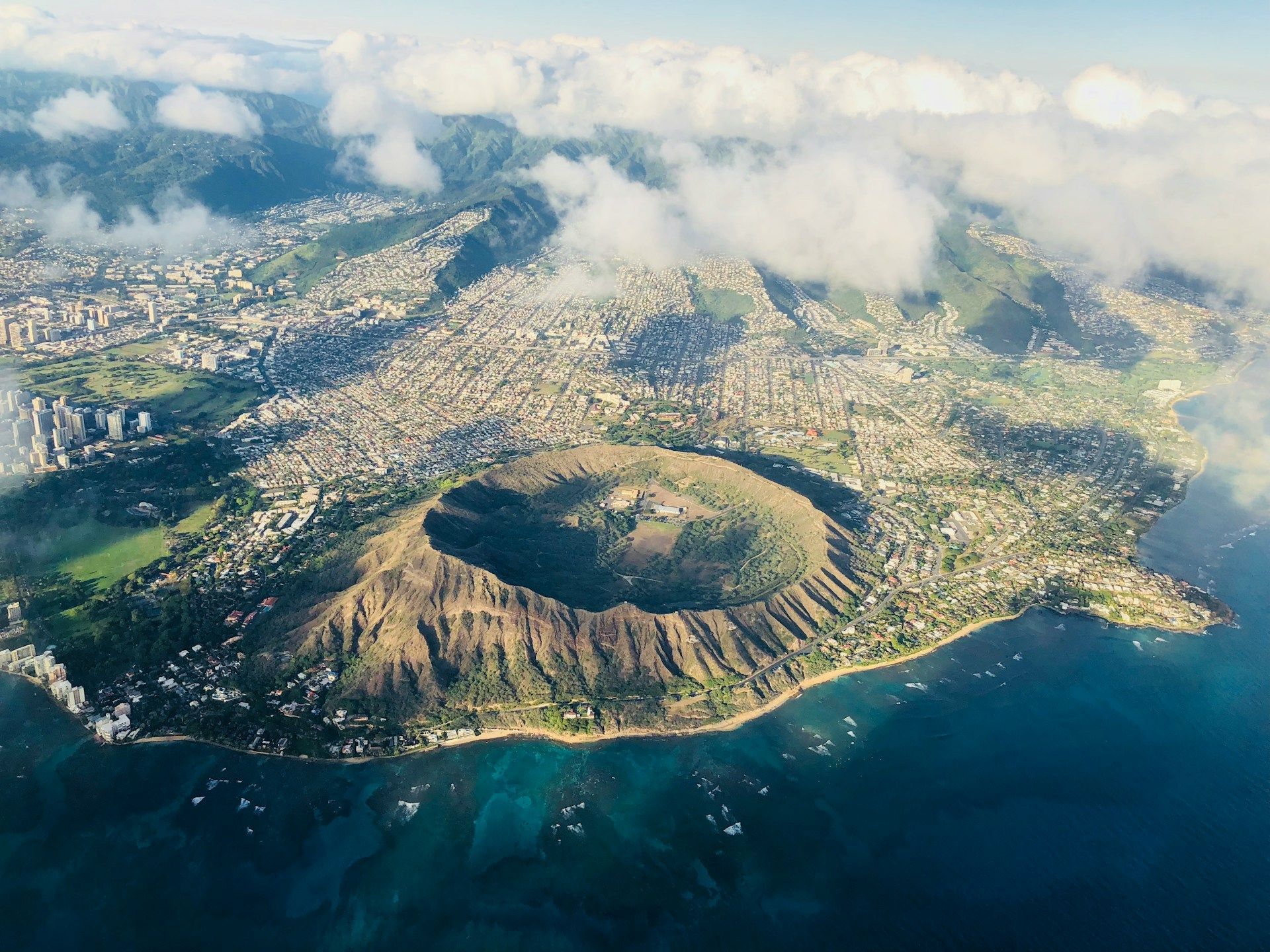 Vista aerea di un grande cratere vulcanico circolare su una costa accanto a una città popolosa e acque blu dell'oceano.