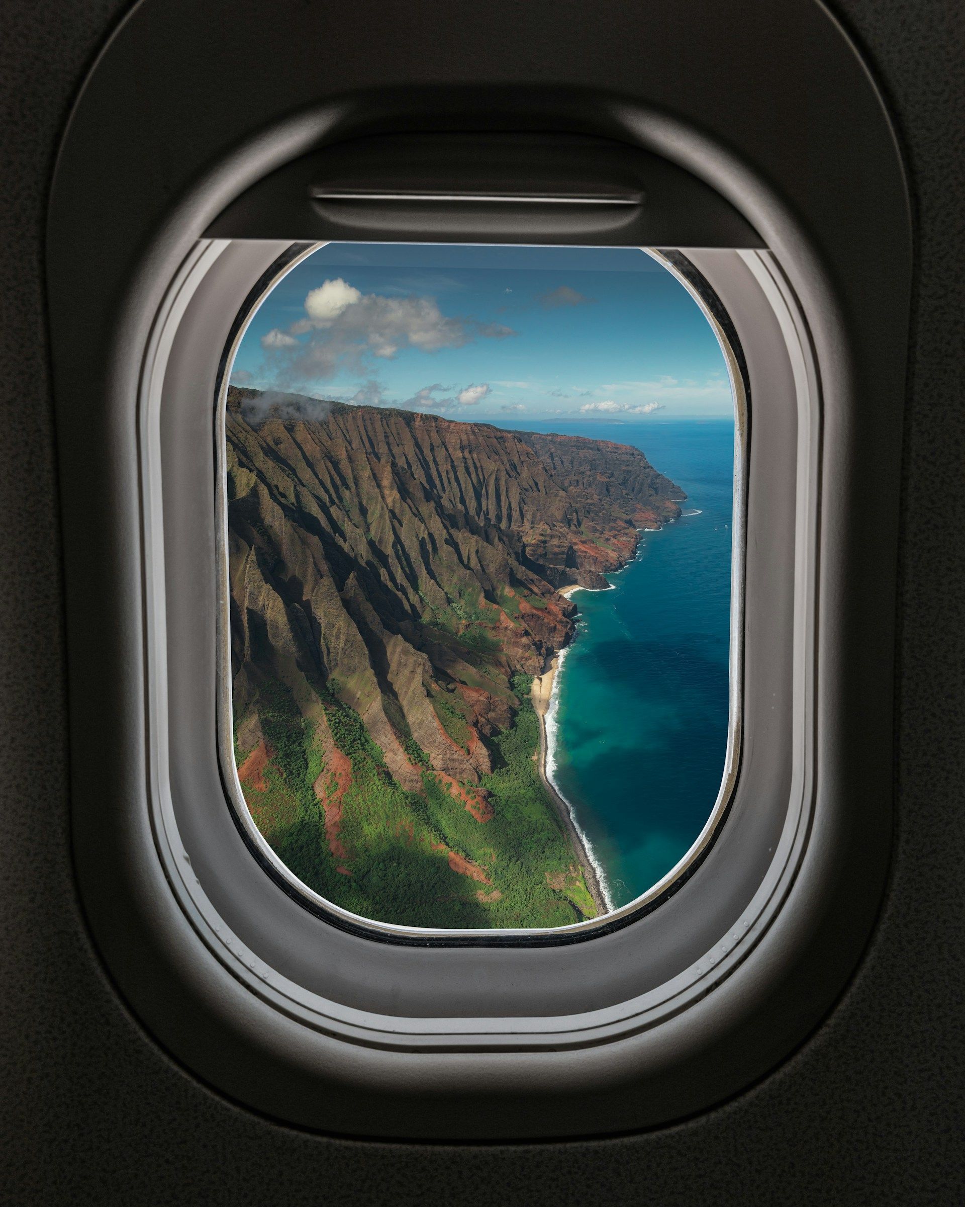Una vista aerea dal finestrino di un aereo di una costa frastagliata e verde che incontra le acque turchesi dell'oceano sotto un cielo blu.